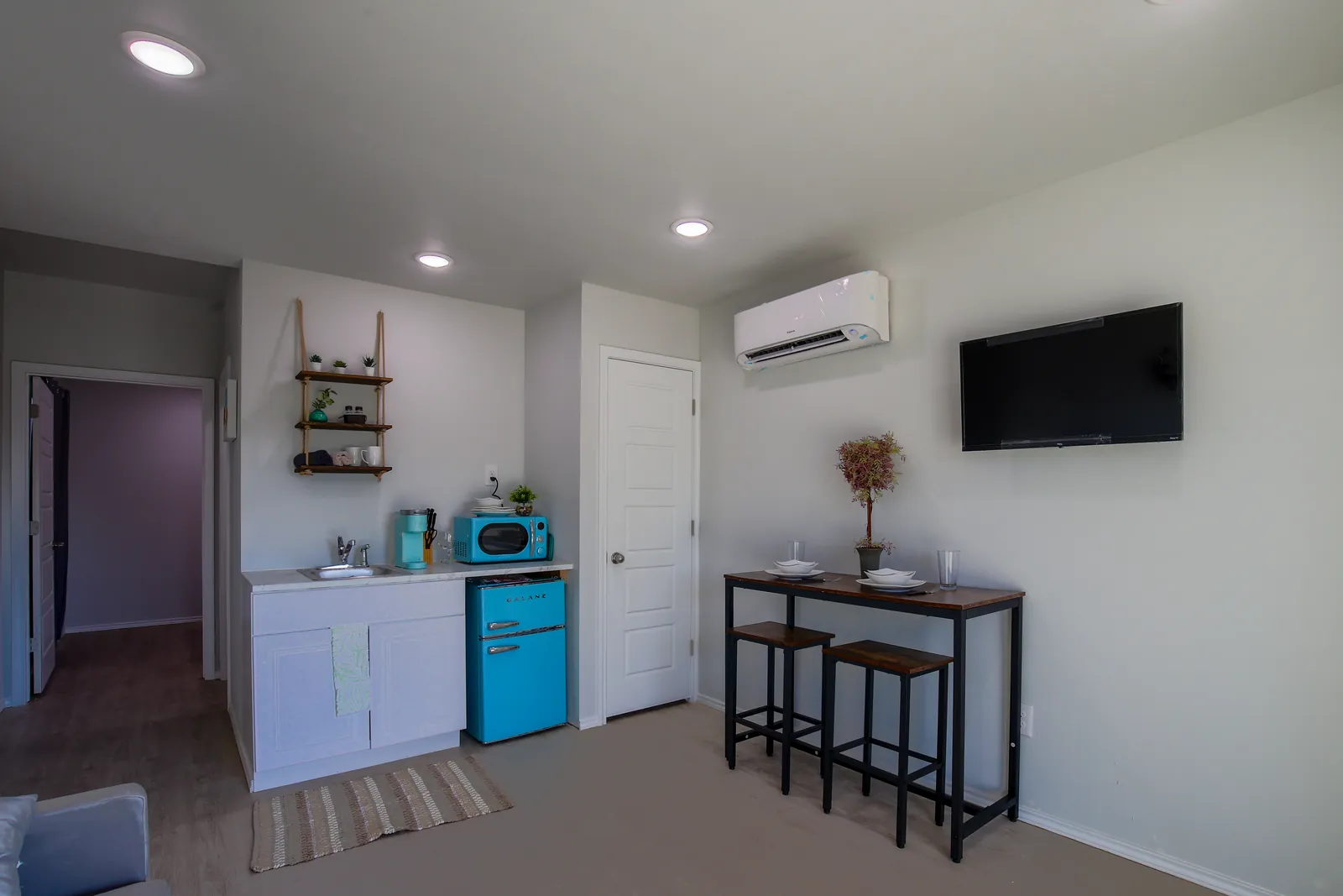 Furnished container-home interior with kitchenette, dining set, and wall-mounted TV